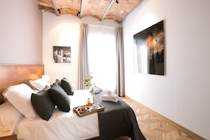 A hotel room with a bed, a tray with croissants and a drink, a vase with flowers, and artwork on the walls. - Serennia Apartments Ramblas-Pl.Catalunya (Barcelona)