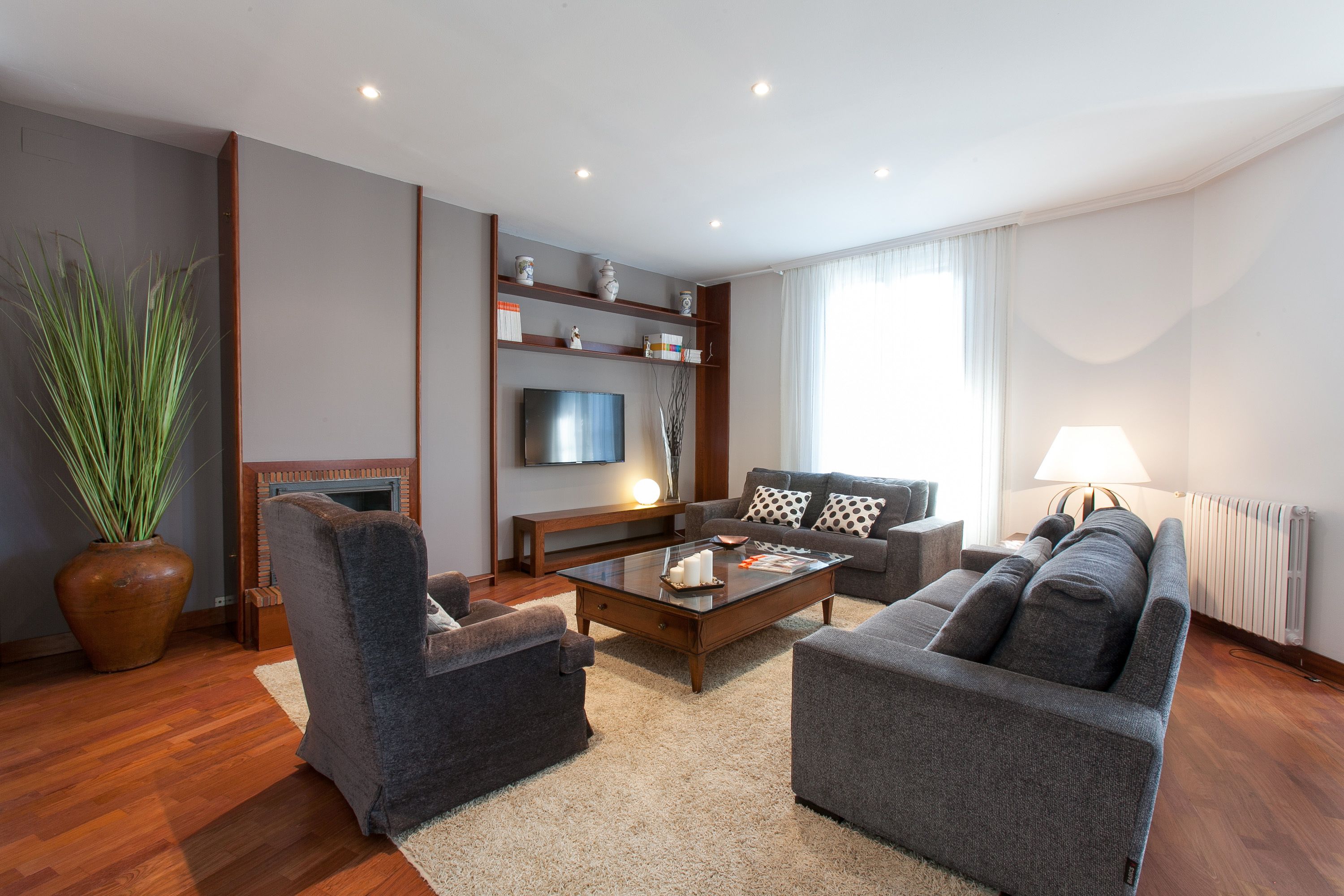 A modern living room with a sofa, armchair, coffee table, and a TV mounted on the wall.
