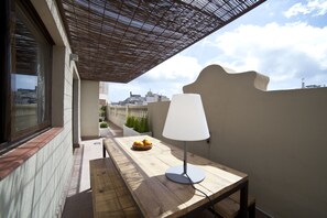 A wooden table with a lamp and a bowl of fruit on a balcony with a view of buildings. - Serennia Apartments Ramblas-Pl.Catalunya (Barcelona)