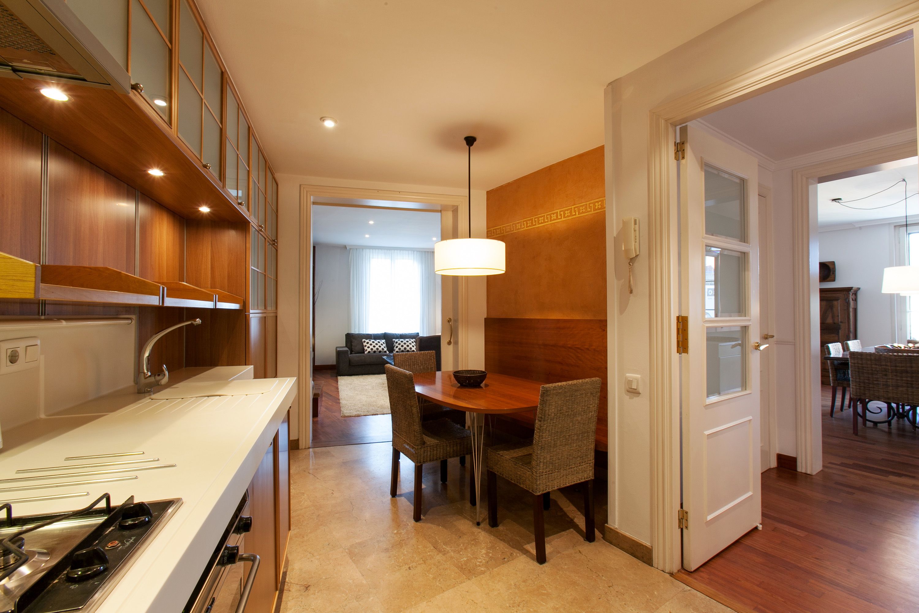 A modern kitchen with a white countertop, wooden cabinets, and a dining area with wicker chairs and a wooden table.