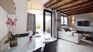 Una sala de estar moderna con comedor, que incluye un sofá, un televisor y una mesa de comedor preparada para cuatro comensales.