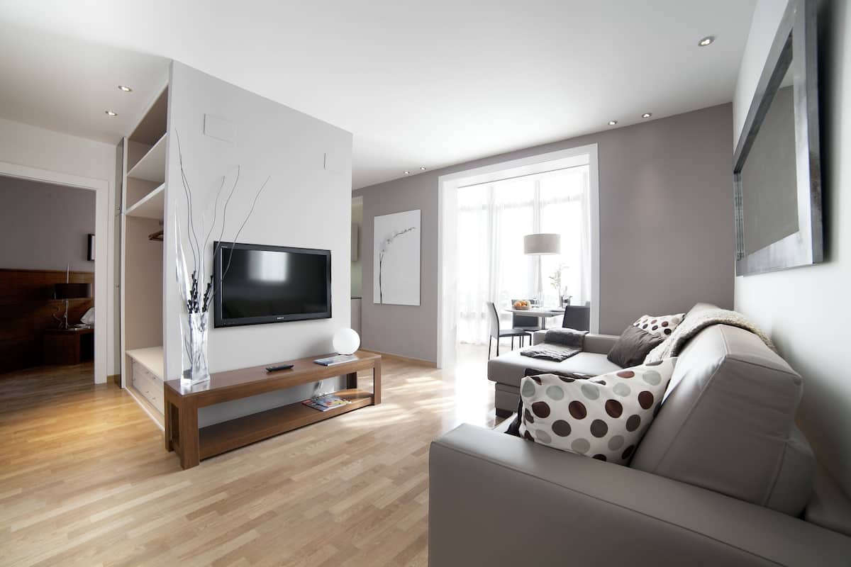 A modern living room with a flat-screen TV, wooden flooring, a sofa with polka dot cushions, and a dining area in the background.