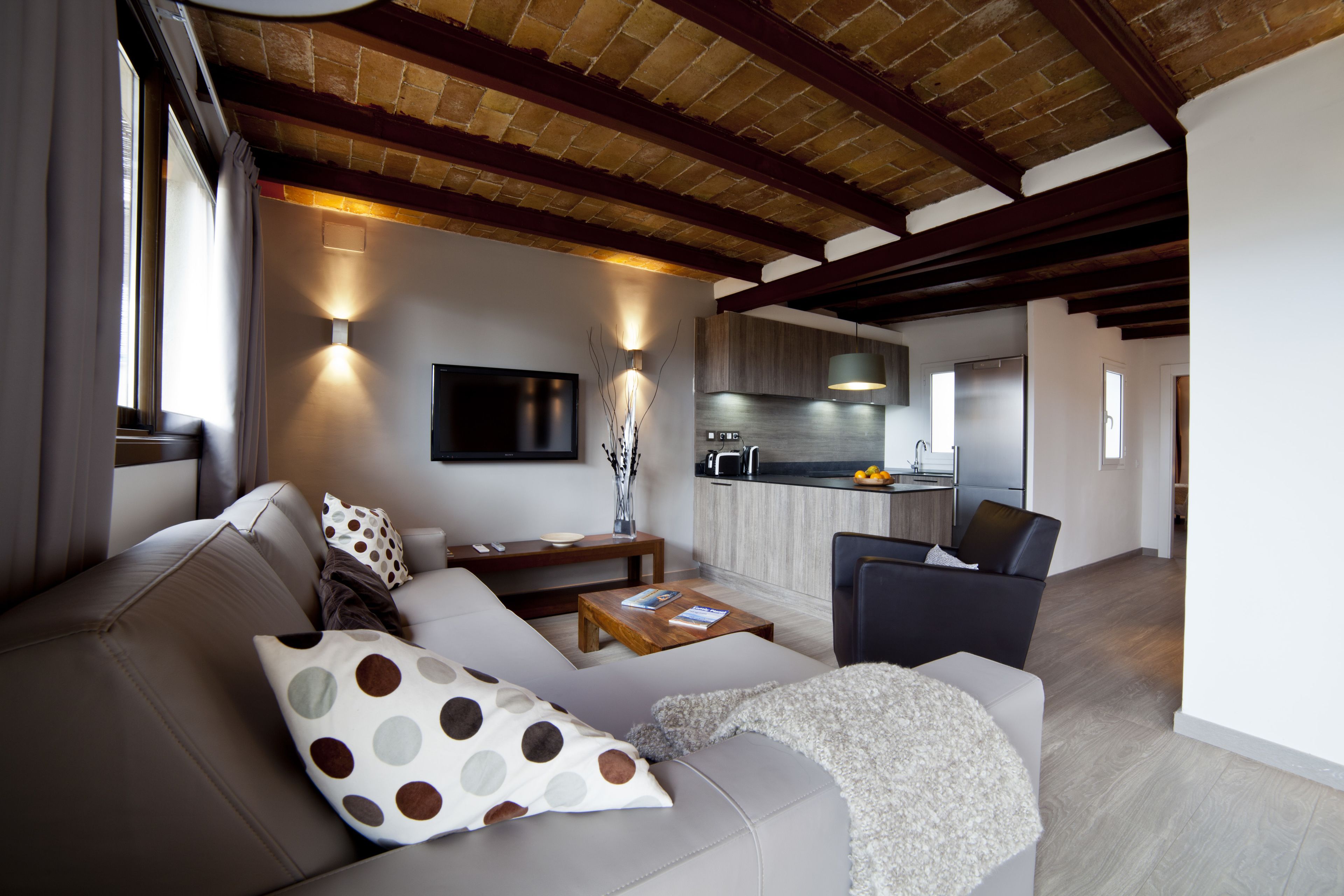 Una sala de estar moderna con un sofá, una mesa de centro y un televisor. Se ve una cocina al fondo.