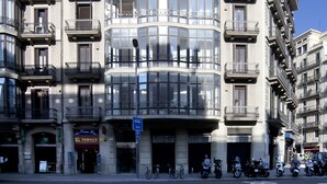 Un edificio de varios pisos con balcones, una entrada en esquina y una fila de motocicletas estacionadas.