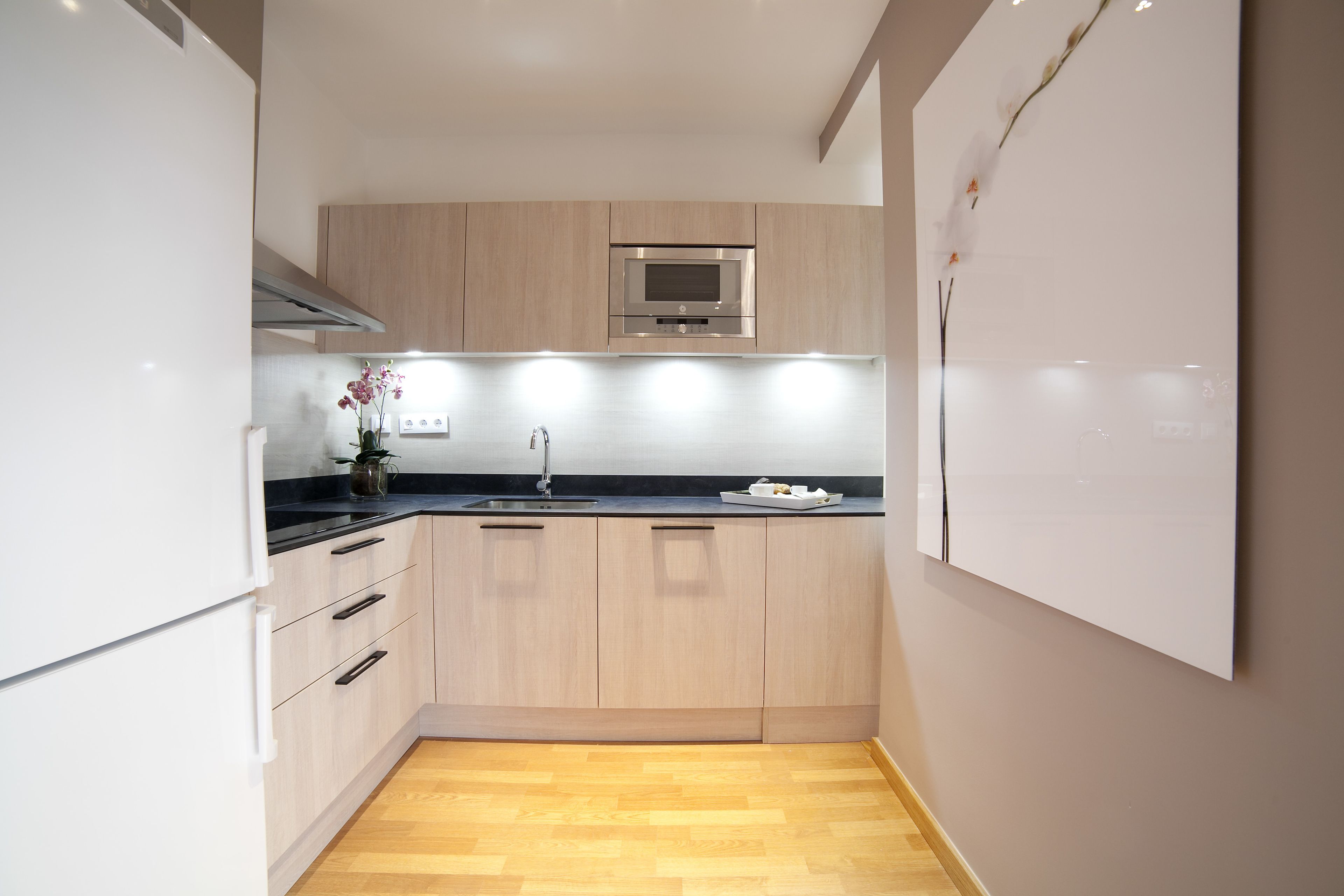 Een moderne keuken met lichte houten kastjes, een oven van roestvrij staal en een zwart aanrecht.