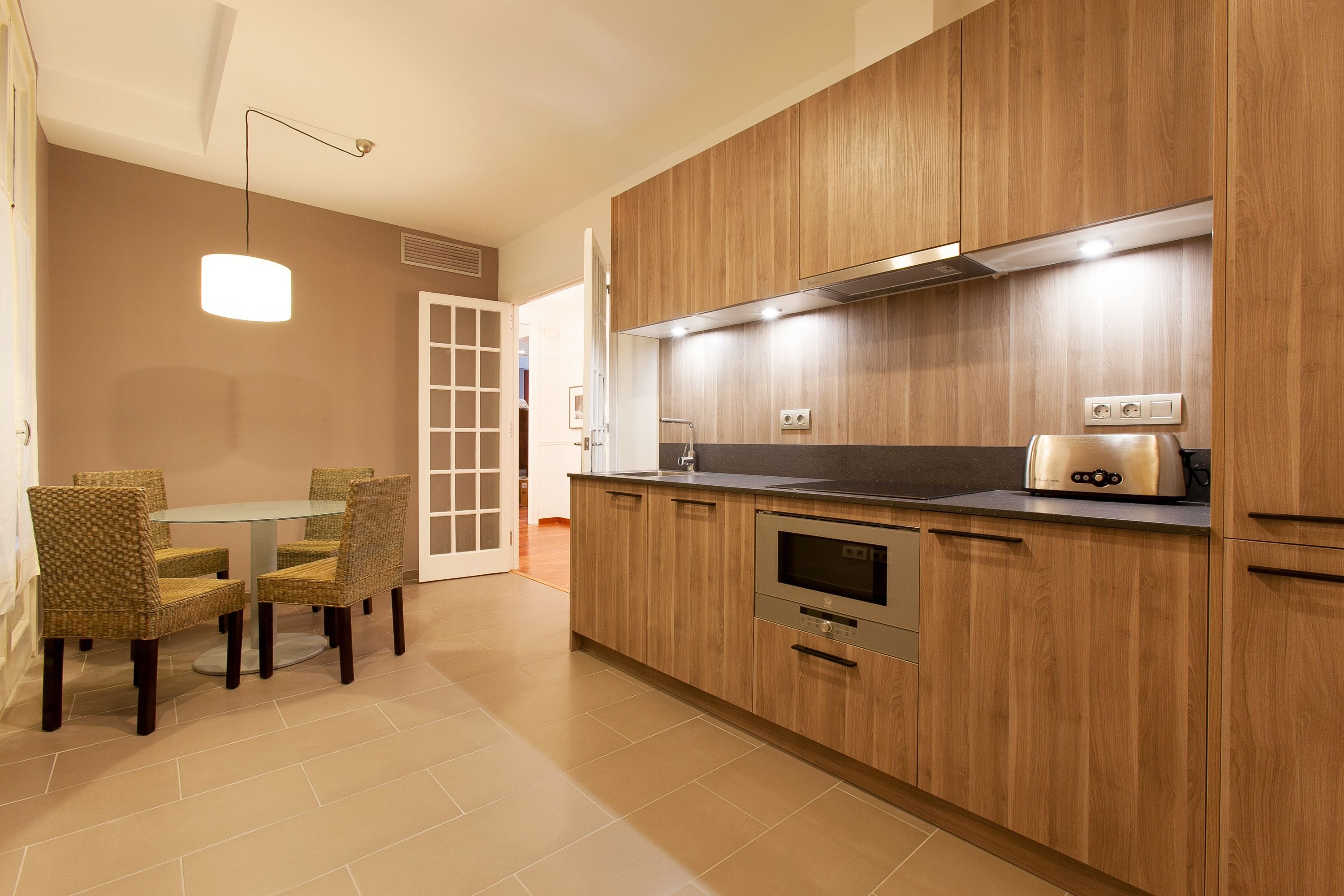Una cocina moderna con armarios de madera, horno empotrado y un comedor con sillas de mimbre.