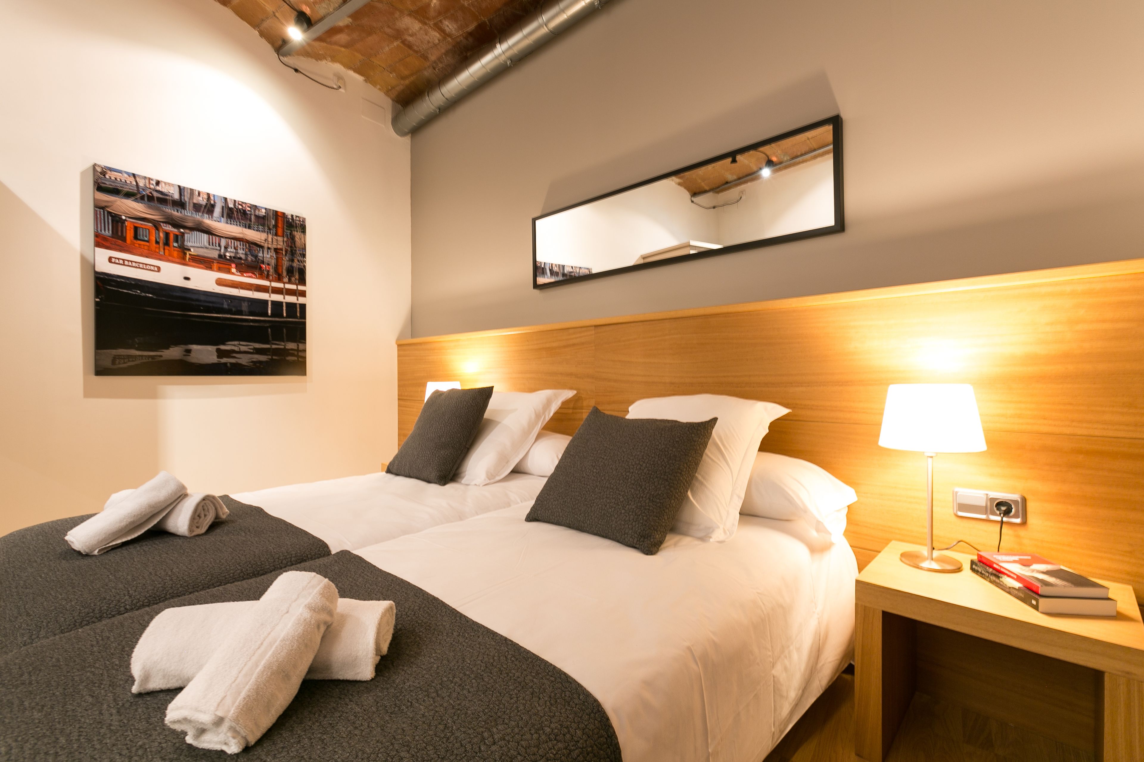 A hotel room with two beds, a wooden headboard, a nightstand with a lamp, and a framed picture on the wall.