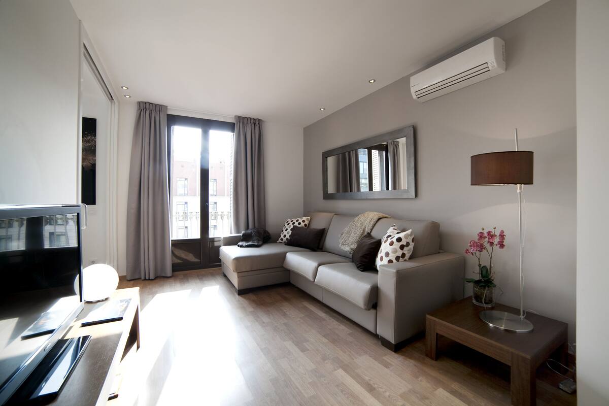 A modern living room with a sectional sofa, a flat-screen TV, a wooden coffee table, and a floor lamp.