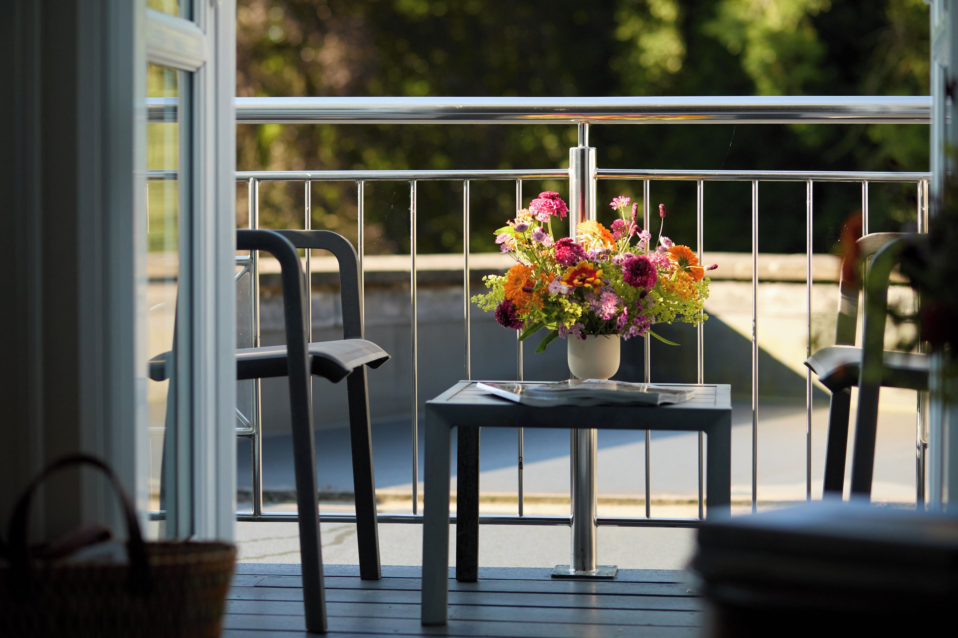 A balcony with a metal railing, a small table with a vase of flowers, and two chairs.