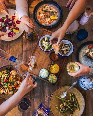 A group of people dining at a wooden table with various dishes, drinks, and a blue and white ceramic jug. - Fermain Valley Hotel (St. Peter Port)