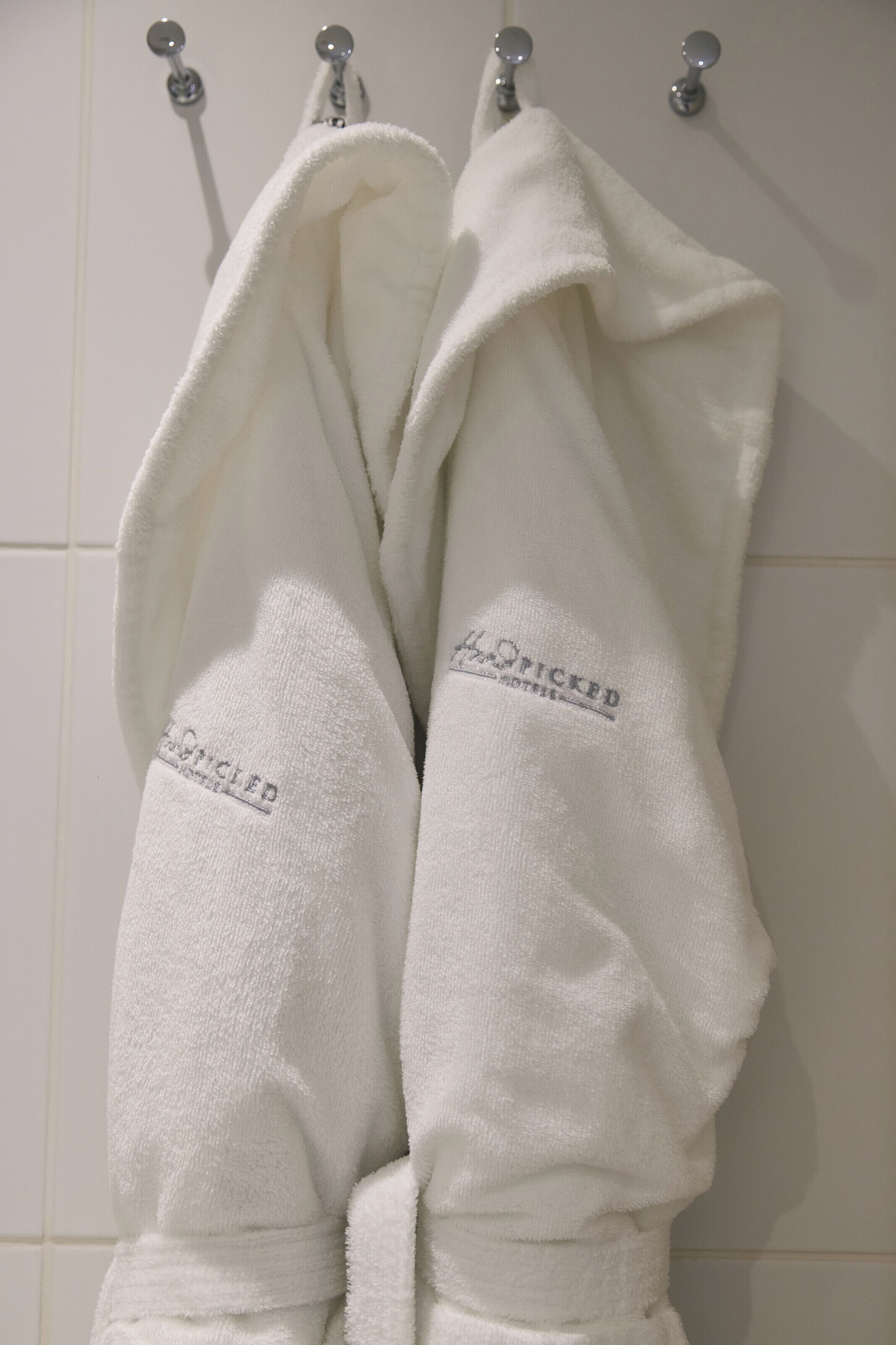 Zwei weiße Bademäntel hängen an einem Metallhaken in einem Badezimmer.