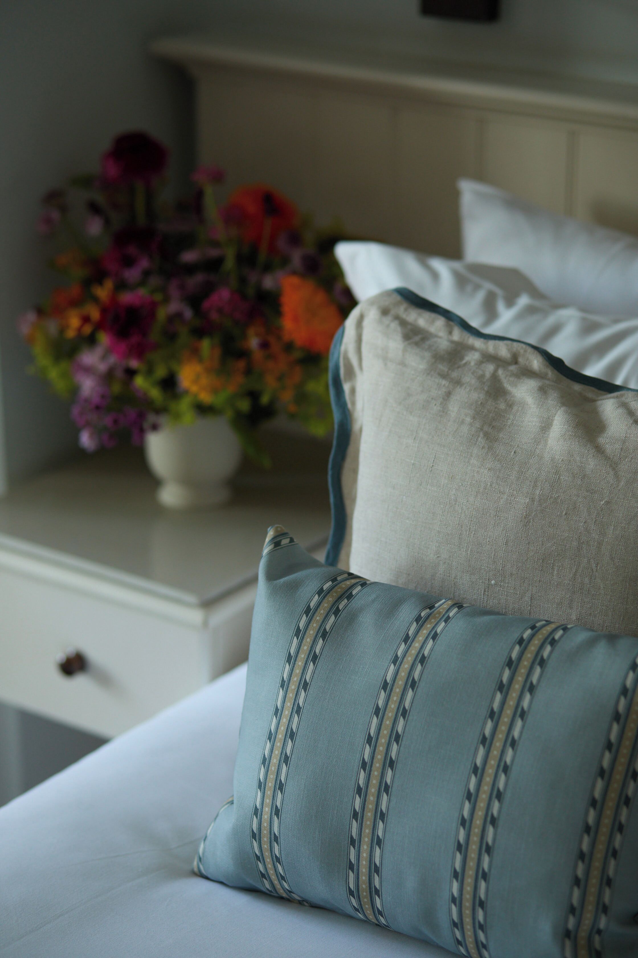 A bed with a pillow and a bedside table with a vase of flowers.