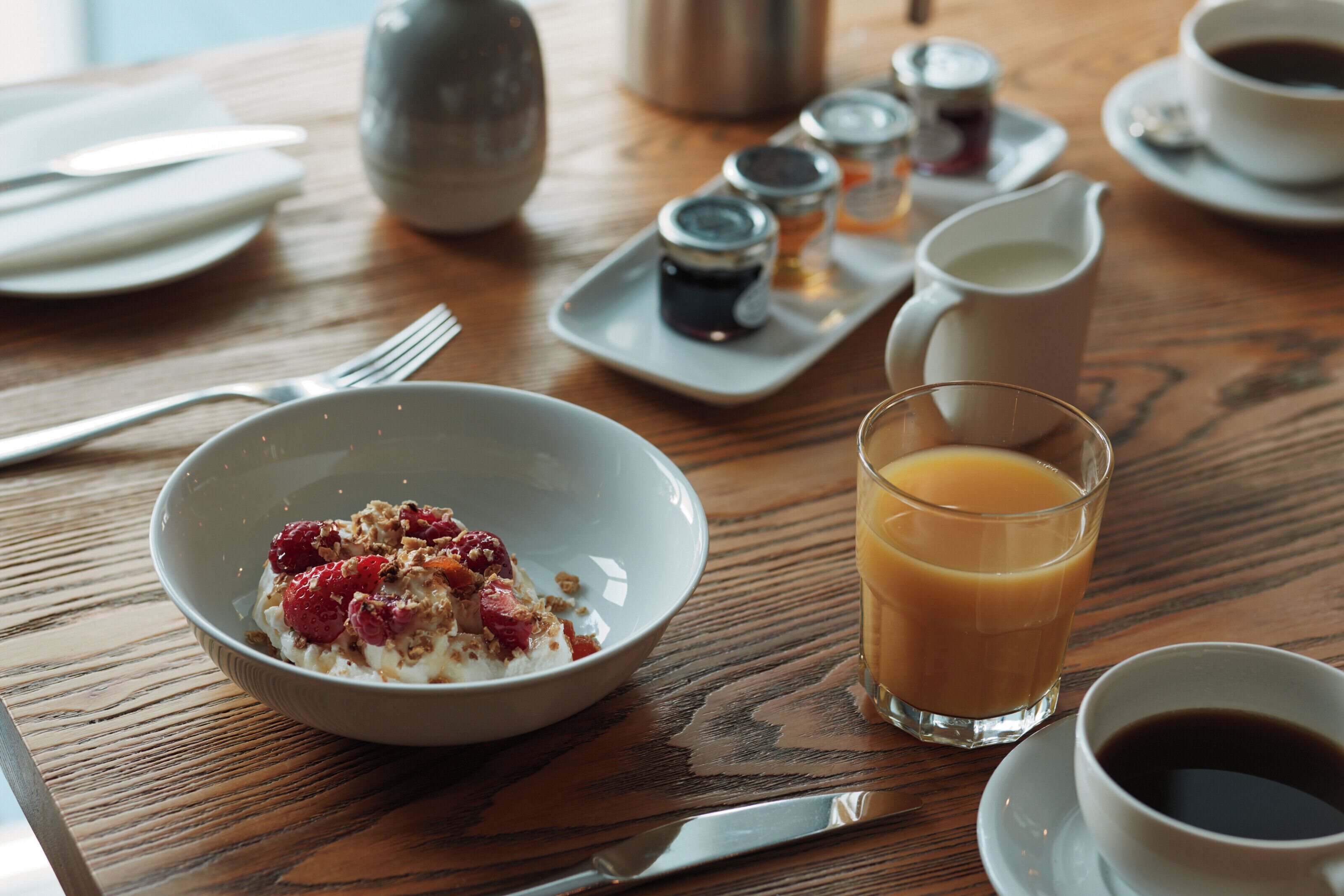 A breakfast setting with a bowl of cereal, a glass of orange juice, and a cup of coffee on a wooden table.