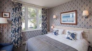 A hotel room with a bed, two bedside lamps, a framed picture on the wall, and a window with curtains. - Fermain Valley Hotel (St. Peter Port)
