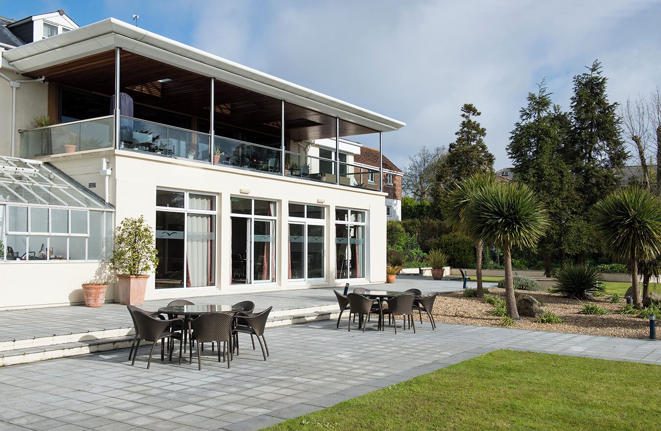 A modern two-story building with a balcony, outdoor seating area, and a well-maintained garden.