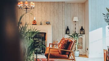 A cozy living room with a wooden floor, a fireplace, a rocking chair, and a large plant.