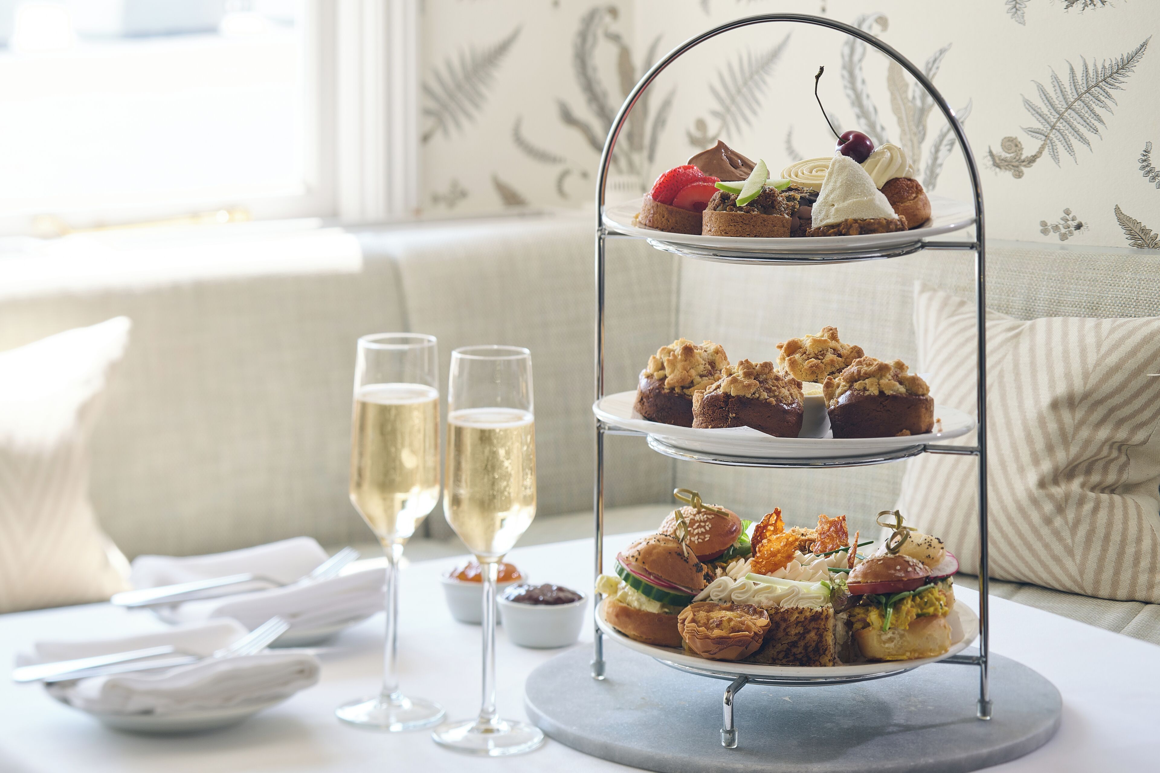 A three-tiered dessert stand with various pastries and a glass of champagne on a table.