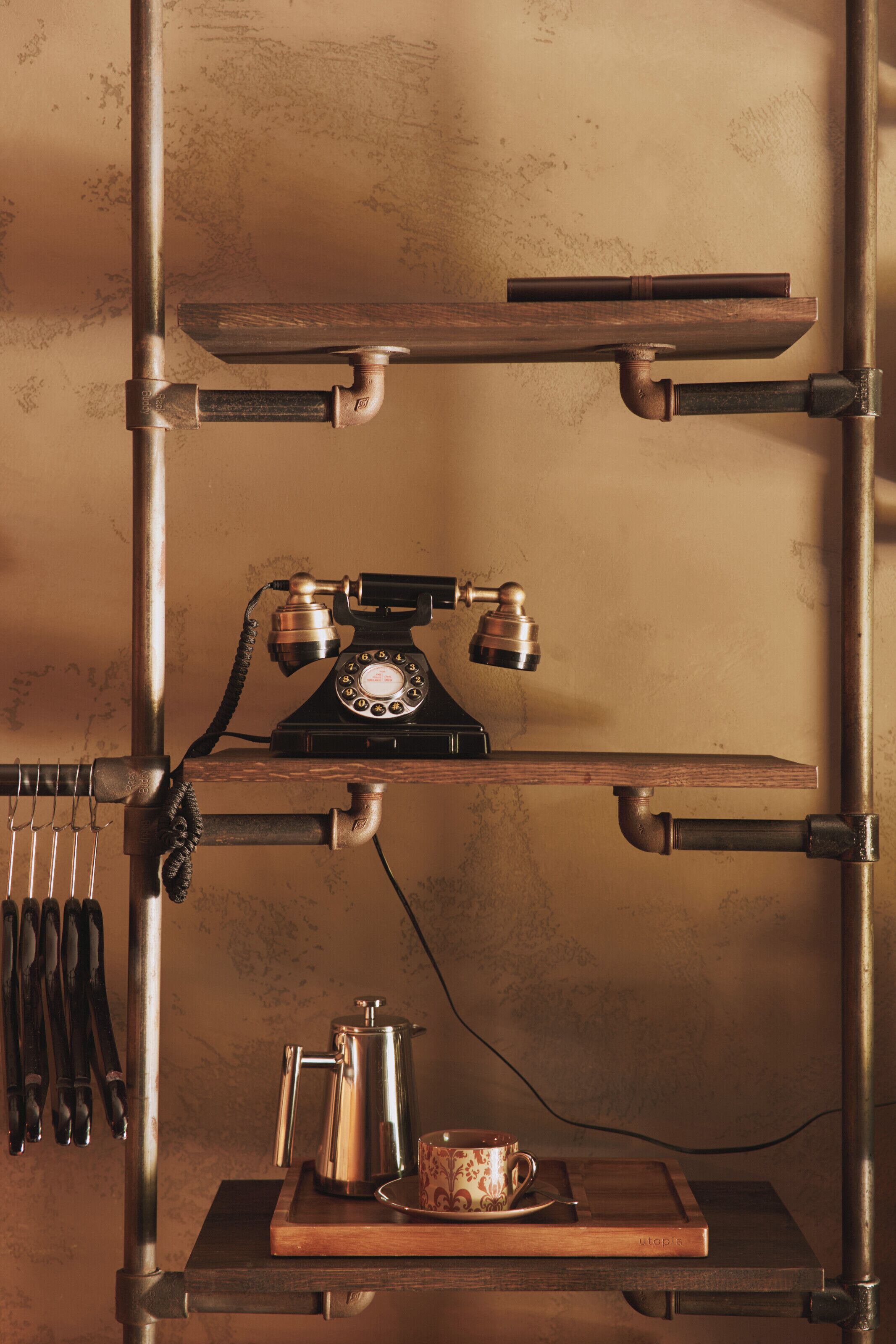 A vintage telephone on a wooden shelf, a metal coffee pot, and a cup on a tray.