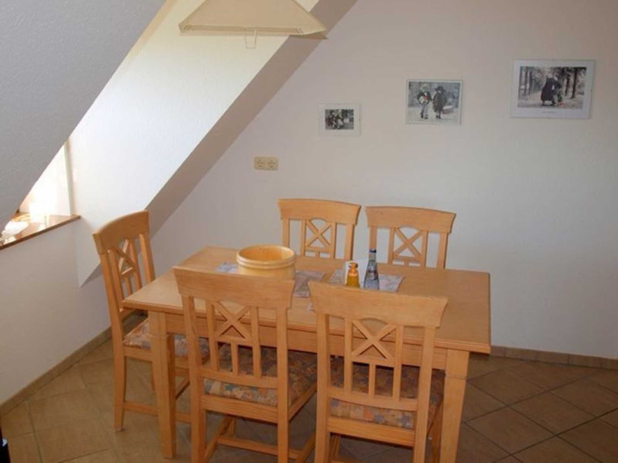 A dining area with a wooden table and chairs, a small window, and three framed pictures on the wall.