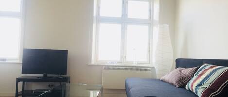 A living room with a glass-top coffee table, a black sofa with a striped pillow, and a television on a black stand.