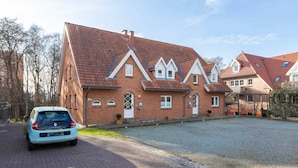 A residential building with a red-tiled roof, multiple chimneys, and a paved driveway. - Apartment 1 (ID 088), Germany (Sankt Peter-Ording)