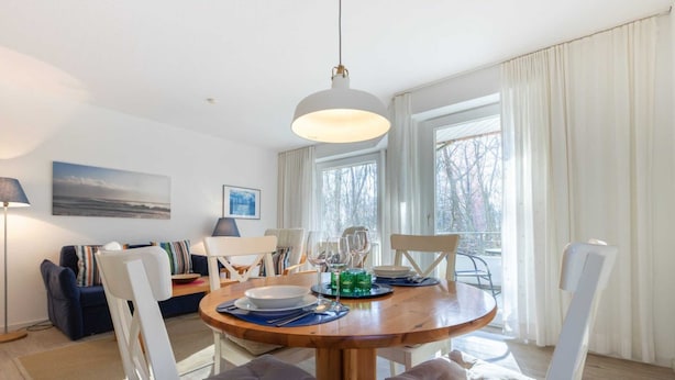 A dining area with a round wooden table, white chairs, and a hanging light fixture. - Apartment 1 (ID 088), Germany (Sankt Peter-Ording)