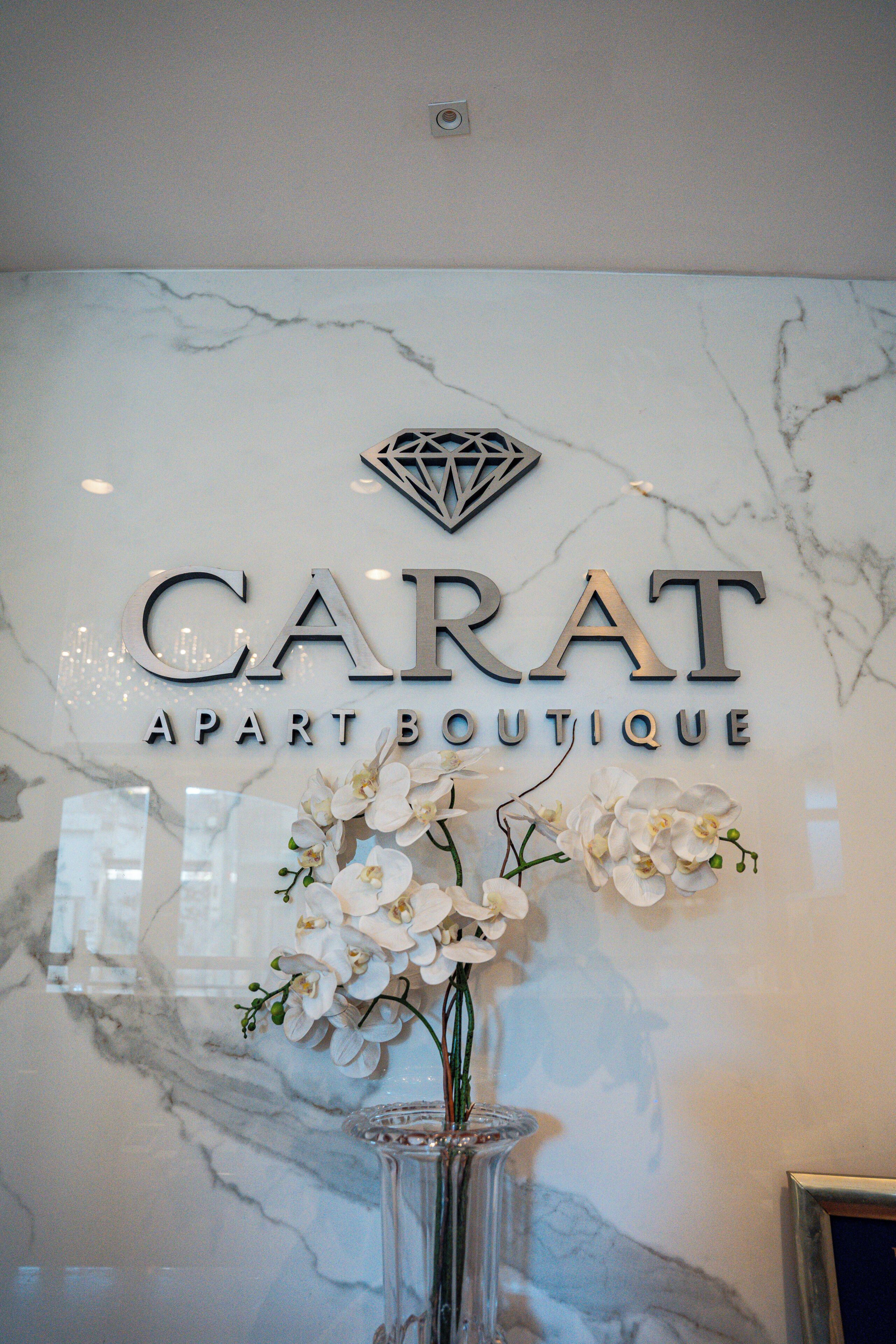 Een marmeren muur met de tekst 'CARAT APART BOUTIQUE' en een decoratief metalen bord erboven.