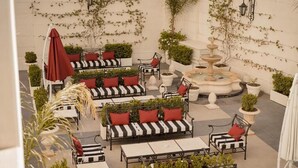 Un patio al aire libre con sofás a rayas, cojines rojos y una fuente central.