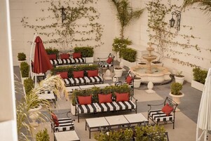 Un patio al aire libre con sofás a rayas, cojines rojos y una fuente central.