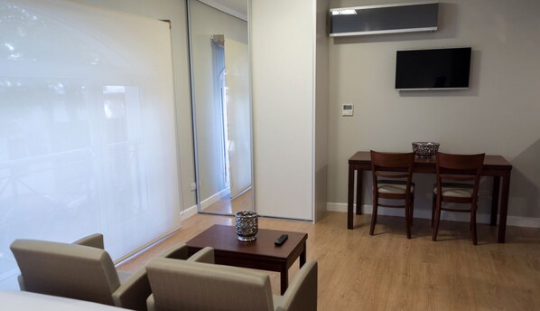 A room with a glass partition, a small table with a remote control, and a TV mounted on the wall. - Carat Apart Boutique (Rosario)