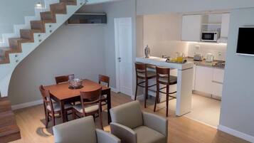 A modern kitchen with white cabinets, a microwave, and a coffee maker. There is a dining area with a wooden table and chairs.