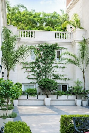 Une cour avec un bâtiment blanc, des plantes en pot et un banc.
