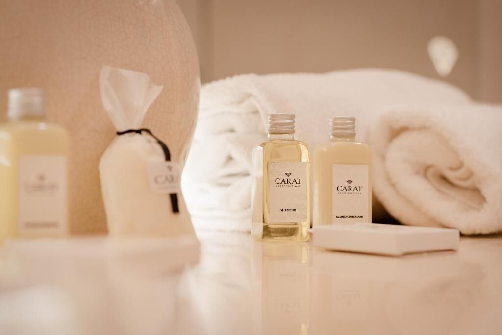 A bathroom with a white towel, two bottles of CARAT shampoo, and a bottle of lotion.