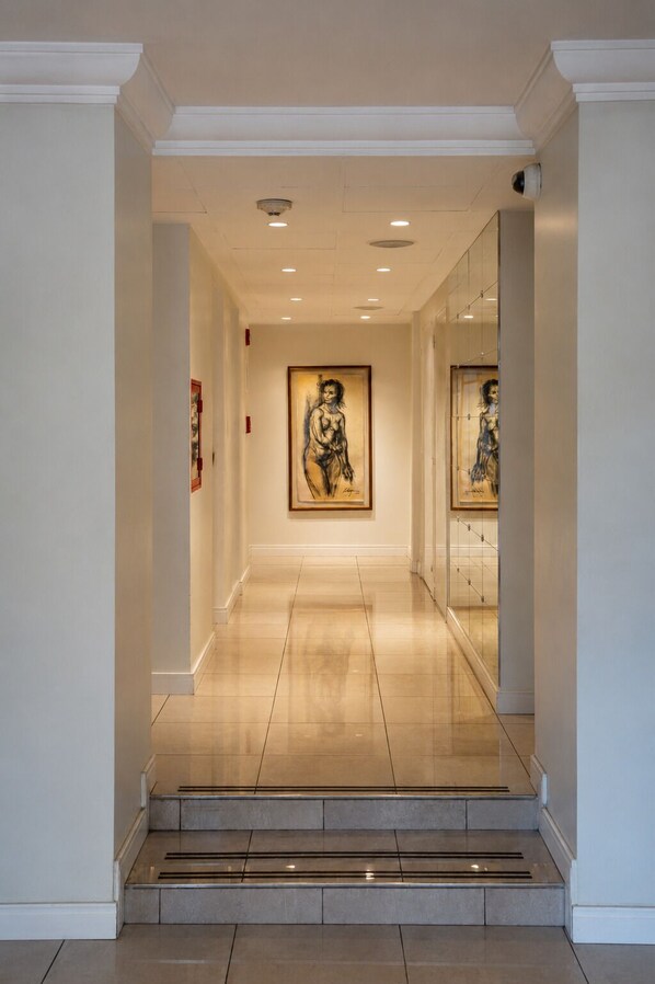 Un couloir avec une œuvre d’art encadrée au mur, une porte vitrée sur la droite et un escalier menant à l’étage supérieur.