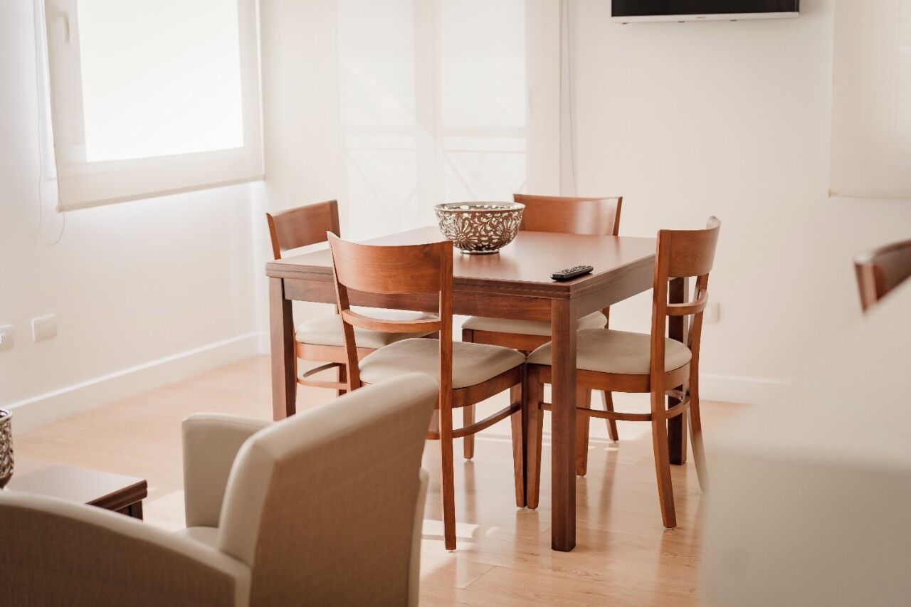 Uma área de refeições com mesa e cadeiras de madeira, uma tigela decorativa e um controle remoto sobre a mesa.