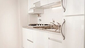 A modern kitchen with white cabinetry, a granite countertop, stainless steel appliances, and a built-in oven. - Carat Apart Boutique (Rosario)