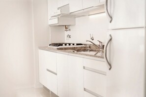A modern kitchen with white cabinetry, a granite countertop, stainless steel appliances, and a built-in oven. - Carat Apart Boutique (Rosario)