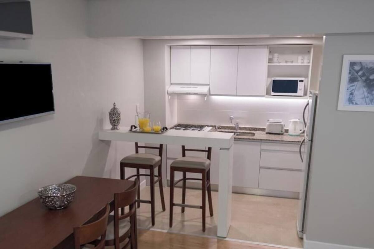 A compact kitchen with white cabinets, a microwave, and a small island with stools.
