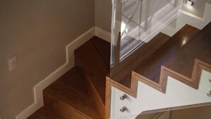 A wooden staircase with a glass railing and a chair at the bottom. - Carat Apart Boutique (Rosario)