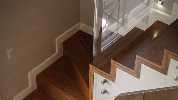 A wooden staircase with a glass railing and a chair at the bottom. - Carat Apart Boutique (Rosario)