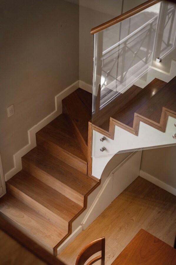 A wooden staircase with a glass railing and a chair at the bottom. - Carat Apart Boutique (Rosario)