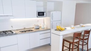 A modern kitchen with white cabinets, a microwave, a refrigerator, a sink, a stove, and a breakfast bar with chairs. - Carat Apart Boutique (Rosario)