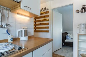 Una cocina compacta con armarios blancos, encimera de madera, una tetera y un colgador para utensilios.