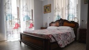 A bedroom with a wooden bed, floral bedding, and curtains with architectural drawings. - Le Camere di Gio (Alba)