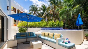 A sunlit outdoor seating area with a sofa, a table, and a blue umbrella. - Casa Susana by Playa Paradise (Playa del Carmen)