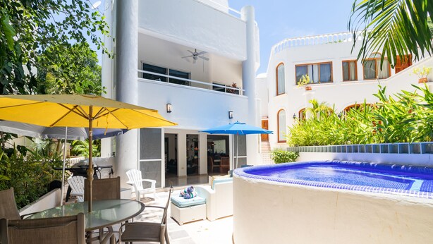 A two-story building with a glass-enclosed balcony, outdoor seating area with a glass table and chairs, and a swimming pool. - Casa Susana by Playa Paradise (Playa del Carmen)