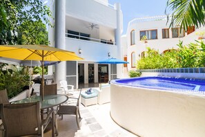 Ein zweistöckiges Gebäude mit einem verglasten Balkon, einer Außenbereich-Sitzgelegenheit mit Glastisch und Stühlen sowie einem Swimmingpool.