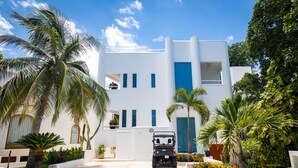 A modern white building with a blue door, surrounded by palm trees and a golf cart in the driveway. - Casa Susana by Playa Paradise (Playa del Carmen)