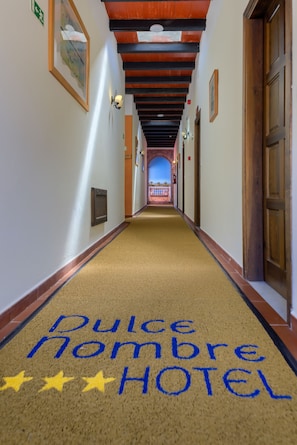 Un pasillo de hotel con una alfombra que dice 'Dulce Nombre Hotel' y un cartel azul a lo lejos.