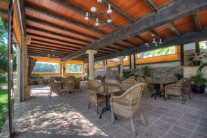 An outdoor patio area with wicker furniture, stone pillars, and a wooden ceiling.